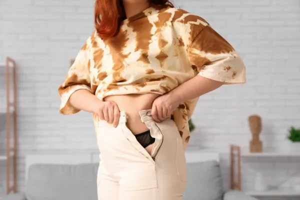 Image of woman trying to do her trousers up after pregnancy weight gain Arnold